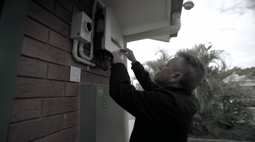 Man stands at solar inverter pointing to button on the system