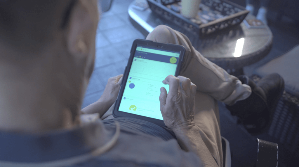 Man sits on chair looking at his solar analytics app on a tablet
