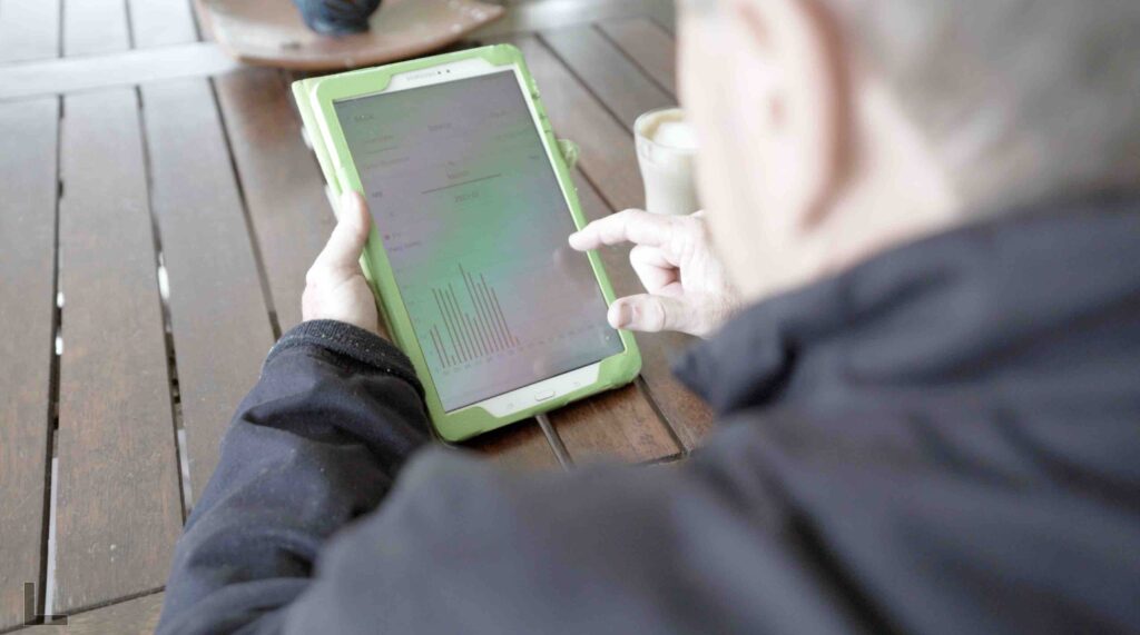 Man sits at table looking at his ipad with solar monitoring displayed on screen