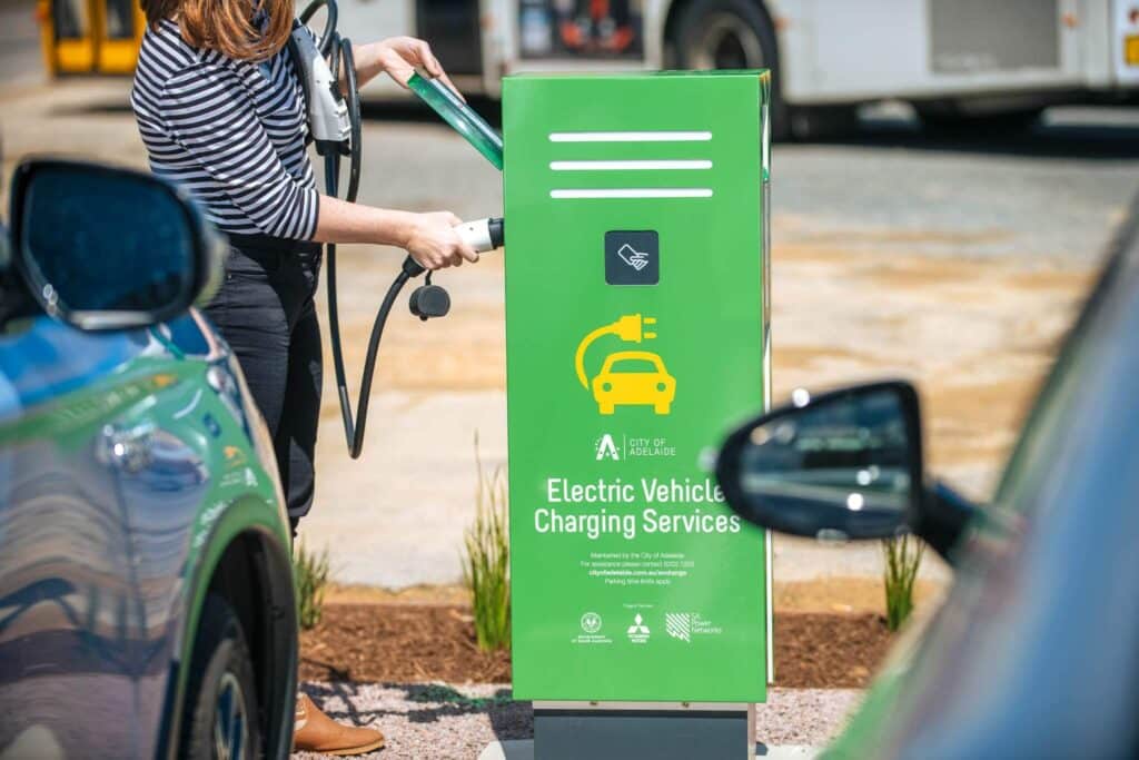 Woman connects electric charger to electric vehicle charging station in the City of Adelaide.